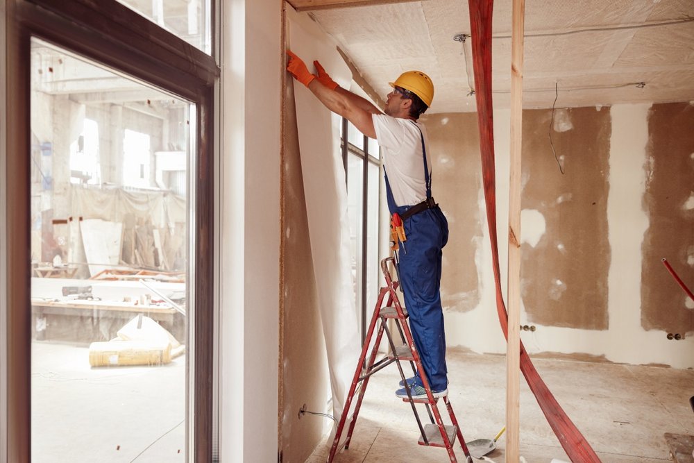 Arbeiter befestigt weiße Trockenbau-Platte an der Wand